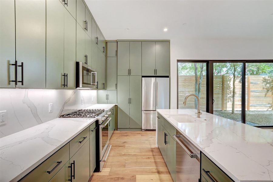 Kitchen featuring appliances with stainless steel finishes, light wood-type flooring, light stone countertops, recessed lighting, and gray cabinetry Kitchen featuring appliances with stainless steel finishes, light wood-type flooring, light stone countertops, recessed lighting, and gray cabinetry