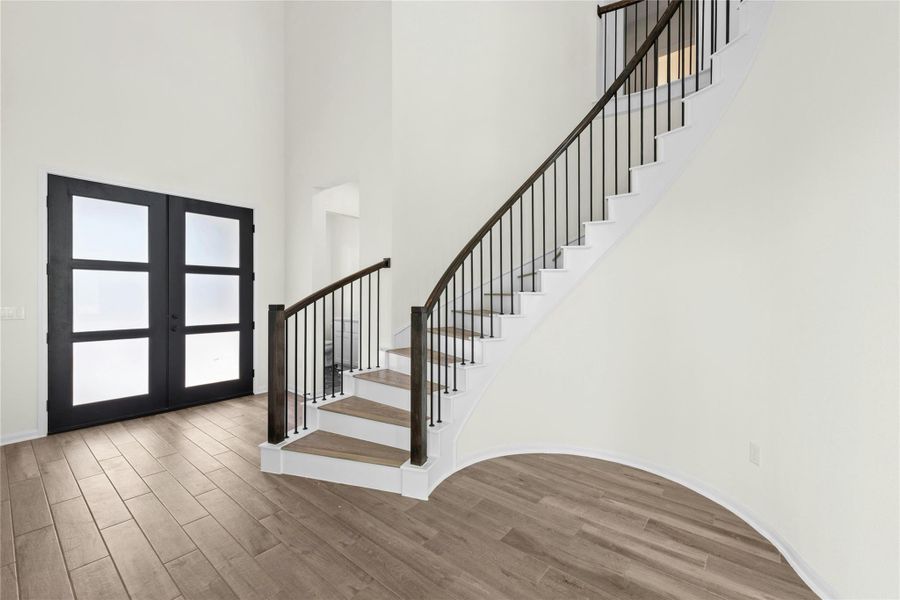 Foyer entrance with stairway, wood finished floors, a towering ceiling, and french doors Foyer entrance with stairway, wood finished floors, a towering ceiling, and french doors