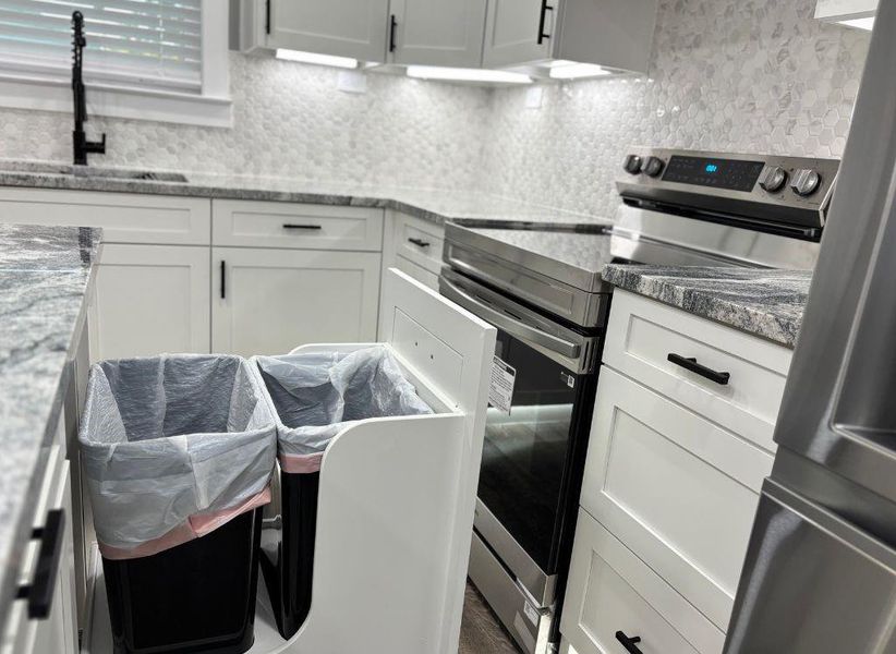 Kitchen with stainless steel appliances, white cabinetry, decorative backsplash, and dark stone counters Kitchen with stainless steel appliances, white cabinetry, decorative backsplash, and dark stone counters