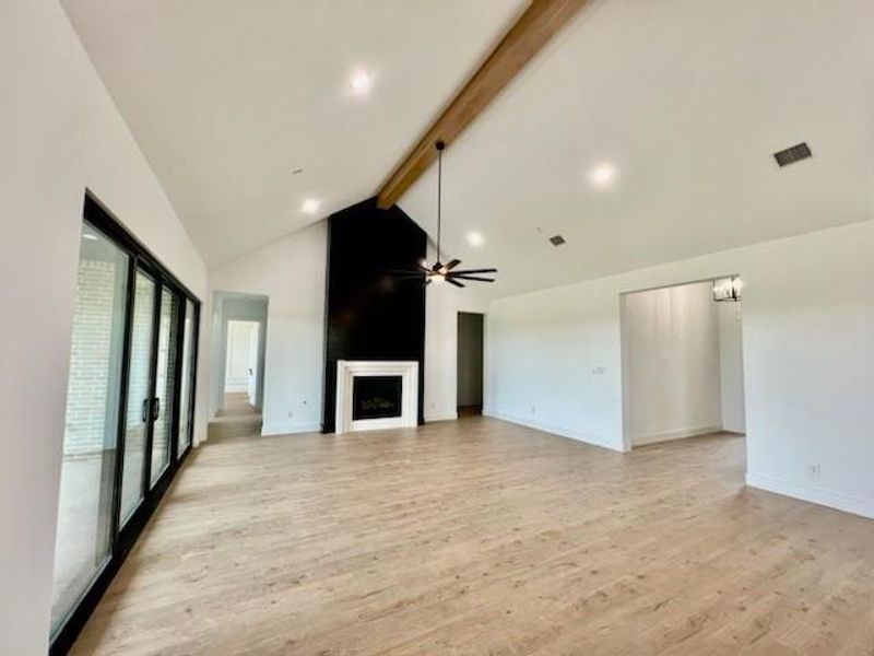 Unfurnished living room with light hardwood / wood-style floors, high vaulted ceiling, ceiling fan, and beamed ceiling