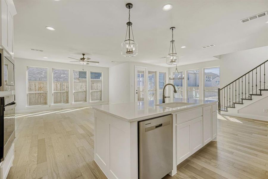 Kitchen featuring white cabinets, stainless steel appliances, open floor plan, light wood-type flooring, and light stone counters