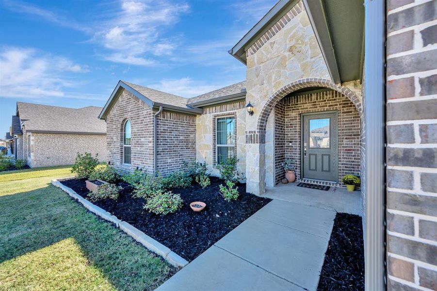 Property entrance with stone siding, brick siding, and a lawn