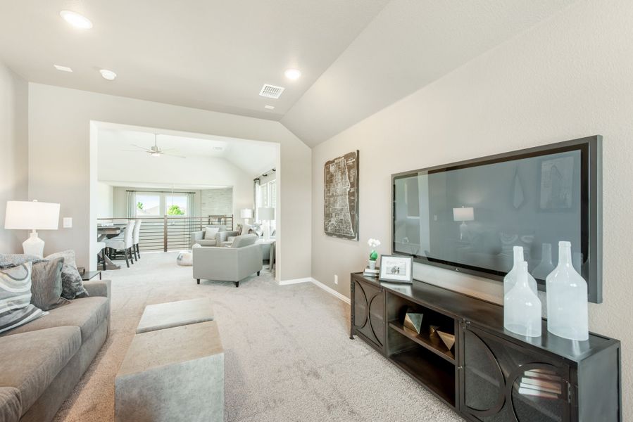 Upstairs bonus room with wall-mounted TV, dark media console, vaulted ceiling, and open view to sitting area