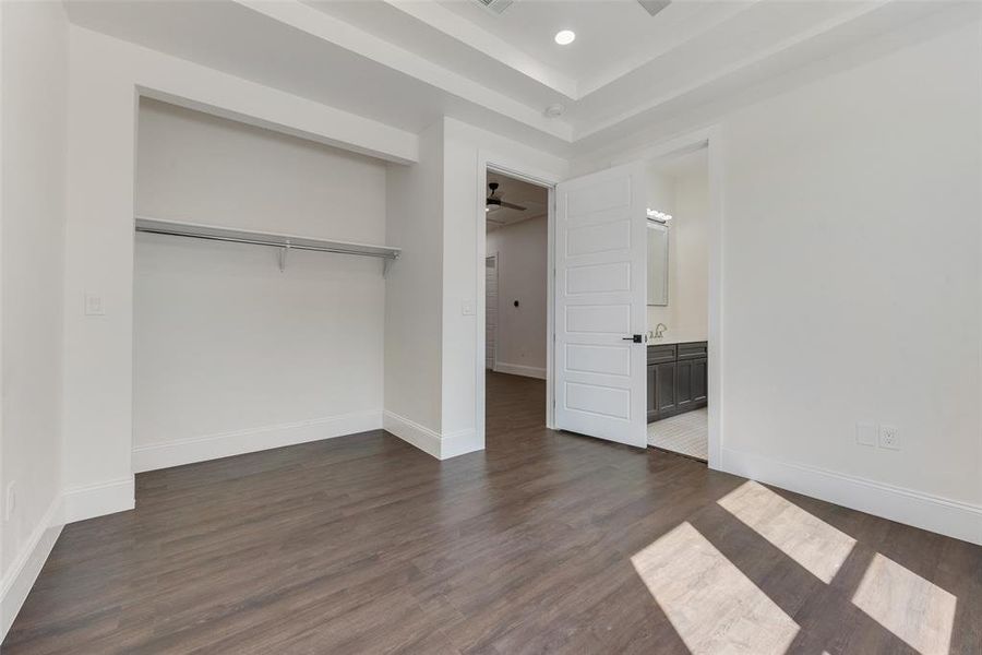 Room featuring dark wood-finish flooring, white baseboards, and a built-in closet with shelving and hanging rod Room featuring dark wood-finish flooring, white baseboards, and a built-in closet with shelving and hanging rod