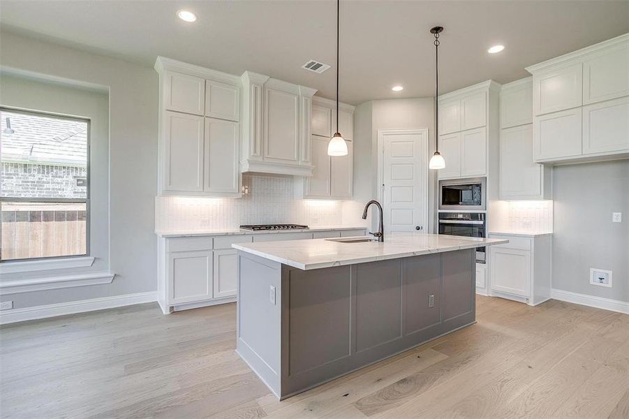 Kitchen featuring light stone countertops, a kitchen island with sink, appliances with stainless steel finishes, and white cabinetry