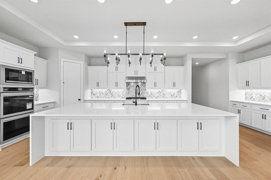 Kitchen with a large island, white cabinets, tasteful backsplash, stainless steel appliances, and light stone countertops