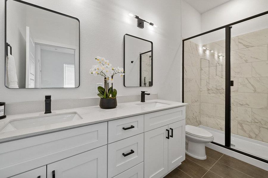 Full bathroom featuring a stall shower, double vanity, and dark tile patterned flooring
