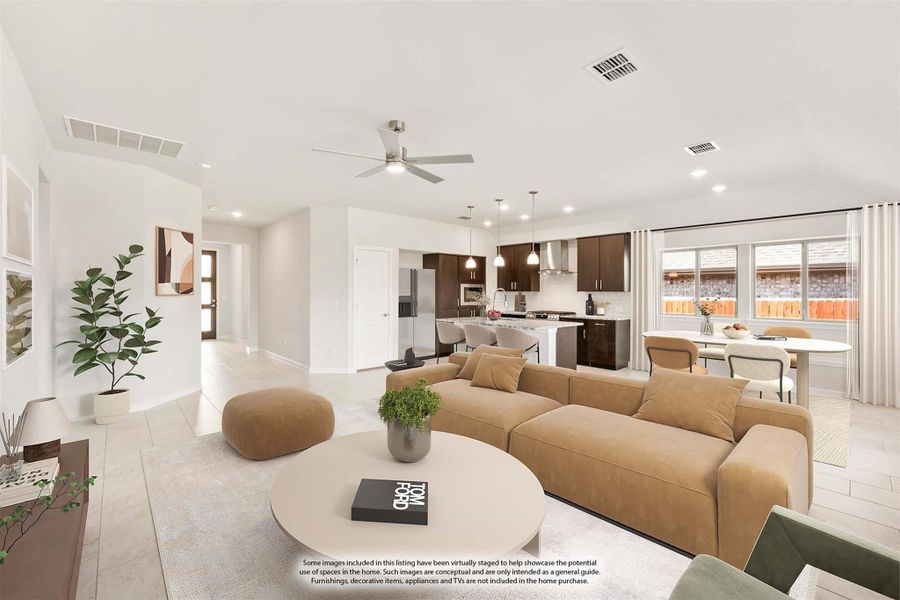 Open-concept living room with tan sectional sofa, ceiling fan, and kitchen visible in background