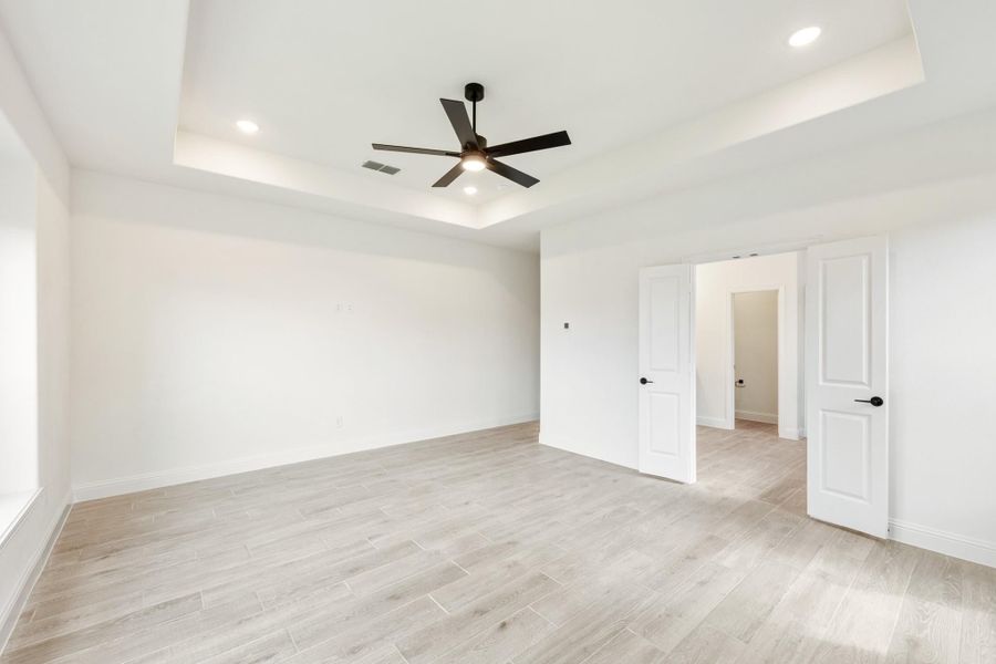 Empty bedroom with tray ceiling, black ceiling fan, light wood floors, and two white doors