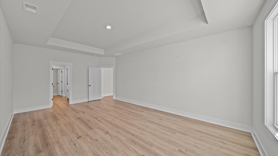 Elegant primary suite with hardwood flooring, tray ceiling, and superior natural light in this accomplished DRB Homes design Elegant primary suite with hardwood flooring, tray ceiling, and superior natural light in this accomplished DRB Homes design