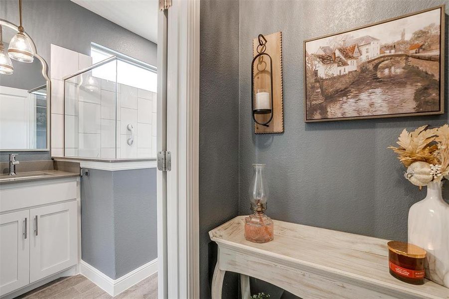 Bathroom with a textured wall, baseboards, a tile shower, and vanity