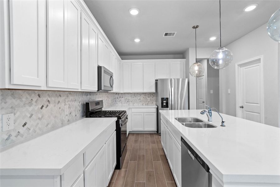 Discover this chef-ready kitchen featuring sleek, shaker-style cabinetry, frost white quartz countertops, and a full suite of stainless steel appliances, including an over-the-range microwave and a side-by-side refrigerator.