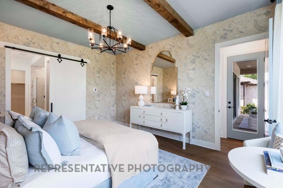 Bedroom with wallpapered walls, dark wood finished floors, a barn door, a chandelier, and beamed ceiling