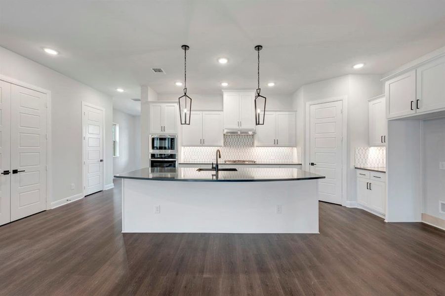 Kitchen featuring white cabinets, tasteful backsplash, stainless steel appliances, decorative light fixtures, and a kitchen island with sink