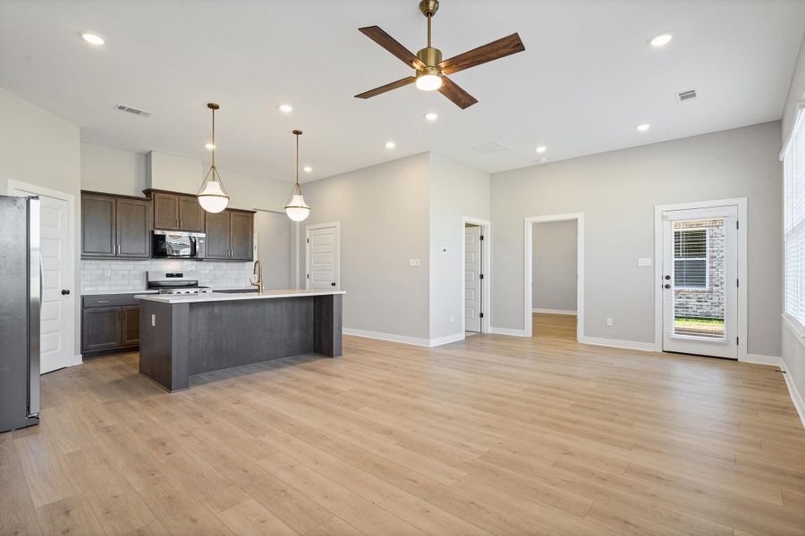 Open-concept living space featuring a kitchen with dark cabinetry, stainless steel appliances, a center island with pendant lighting, and light wood-finish flooring throughout