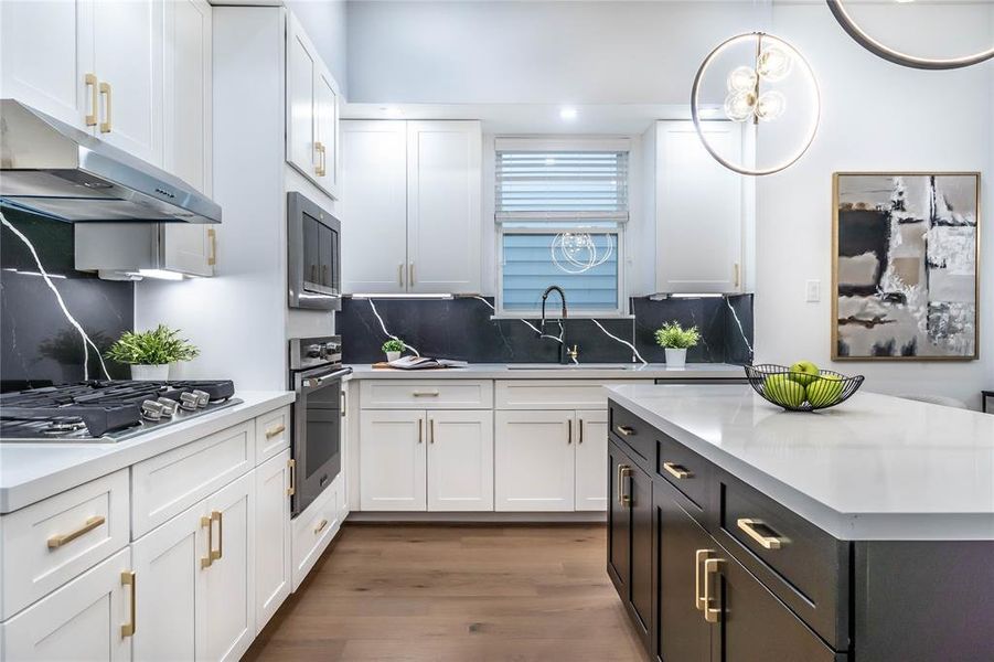 Corner view of the kitchen from the garage entry, featuring shaker-style cabinet doors, gold cabinet pulls, Quartz countertops, and under-cabinet lighting with plugs.