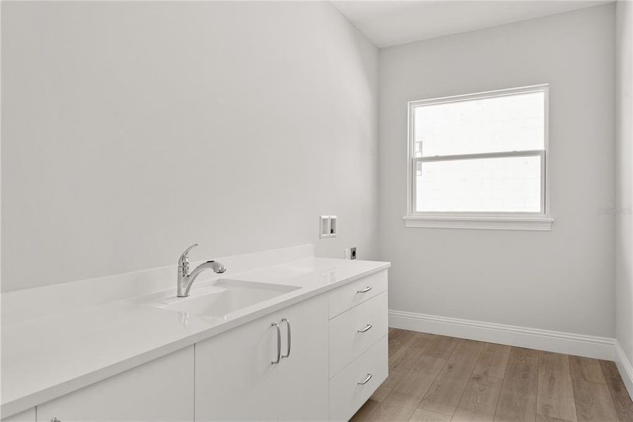 Bright and efficient downstairs laundry room equipped with a utility sink, generous counter space for folding, and ample storage in white cabinetry.