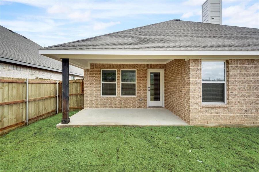 Rear view of house with a shingled roof, a patio, brick siding, and a chimney