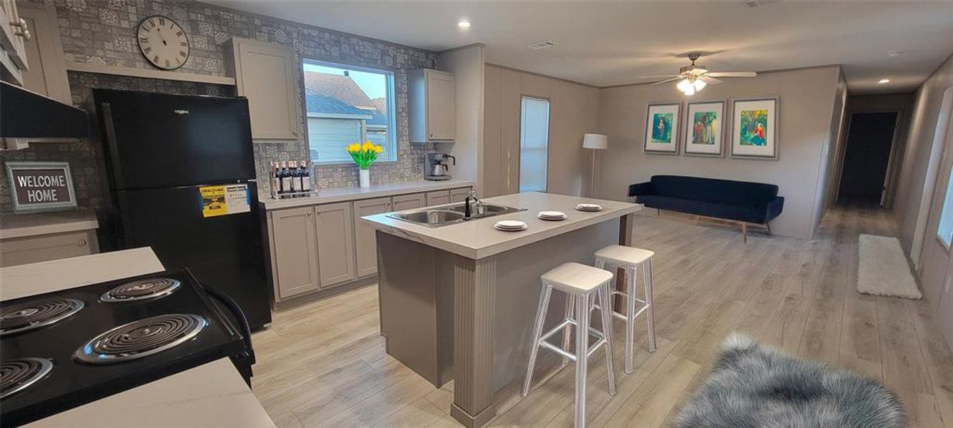 Kitchen with light wood-style flooring, black appliances, light countertops, and a sink