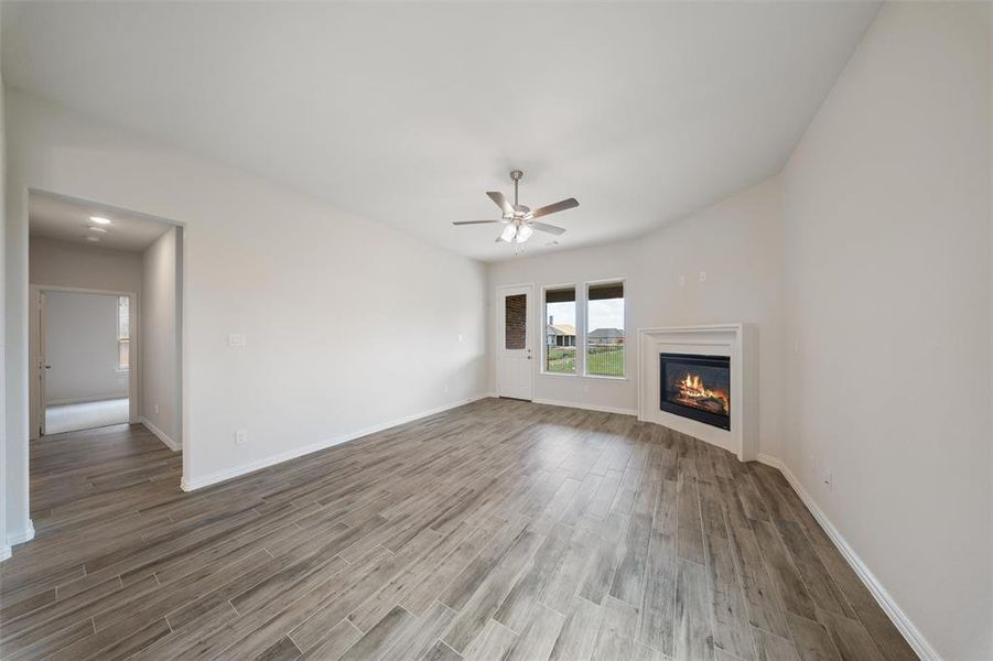 Unfurnished living room featuring ceiling fan, wood finished floors, and a glass covered fireplace