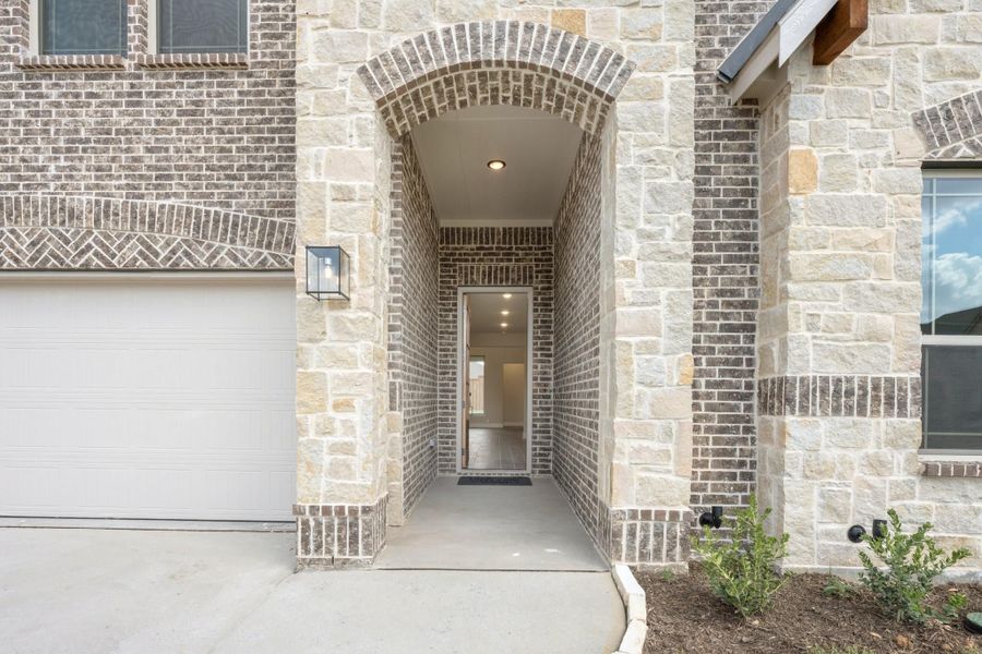 Home entrance with arched brick and stone surround, covered walkway, and front door next to a garage.