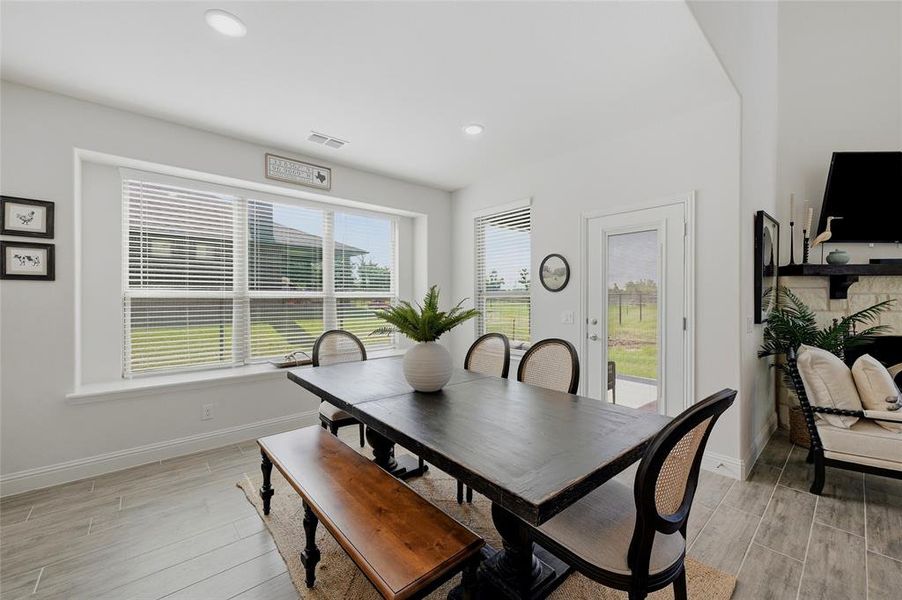 Open-concept dining area featuring wood-finish flooring, a large window with horizontal blinds, and a glass-paneled exterior door