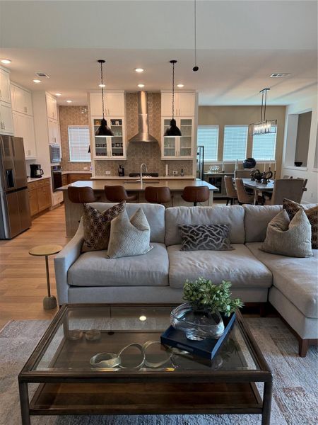 Open-concept living area featuring a modern kitchen with a extended island, pendant lighting, and stainless steel appliances, seamlessly flowing into a cozy living space with a plush sofa and stylish decor and dining area.
