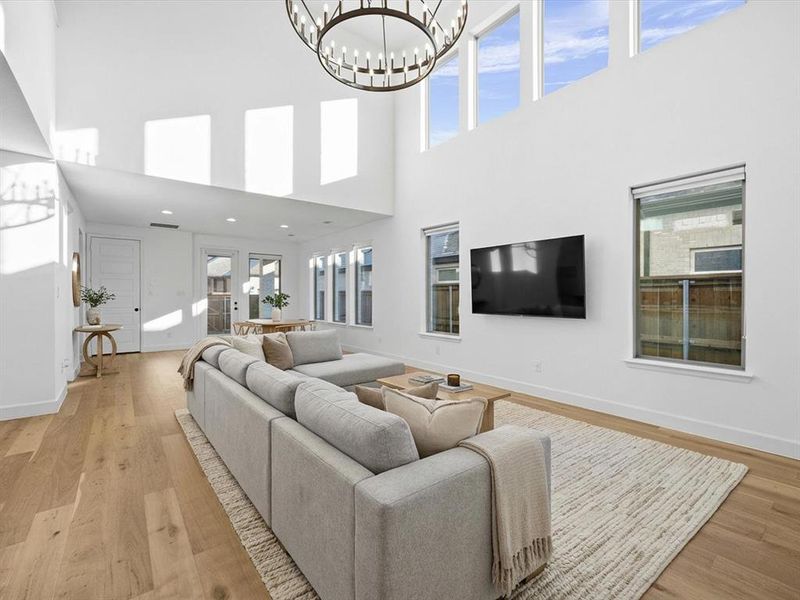 Living room featuring light wood-type flooring, a chandelier, and a towering ceiling Living room featuring light wood-type flooring, a chandelier, and a towering ceiling