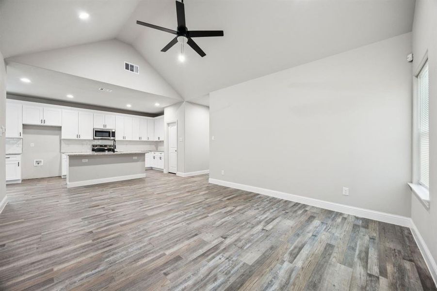 Family with view of kitchen with high vaulted ceiling, light wood-style flooring, ceiling fan, and recessed lighting Family with view of kitchen with high vaulted ceiling, light wood-style flooring, ceiling fan, and recessed lighting