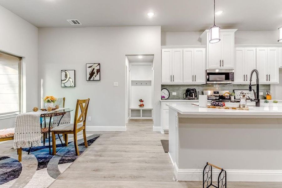 Kitchen with sink, hanging light fixtures, light hardwood / wood-style flooring, tasteful backsplash, and white cabinetry