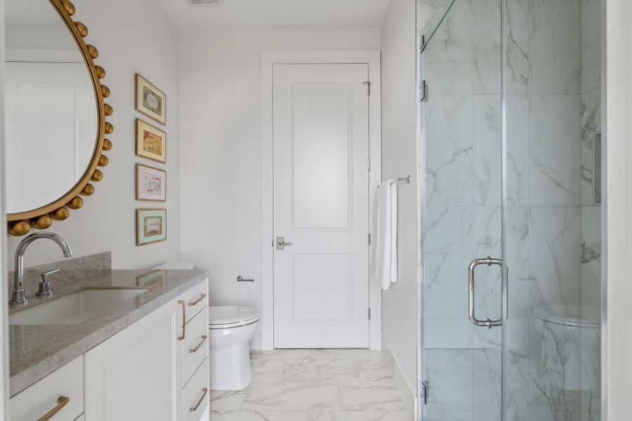 This bathroom features a modern design with a glass-enclosed tiled shower, a sleek vanity with a stone countertop, and elegant fixtures. The space is bright and inviting, with tasteful wall art and a large, decorative mirror. This bathroom features a modern design with a glass-enclosed tiled shower, a sleek vanity with a stone countertop, and elegant fixtures. The space is bright and inviting, with tasteful wall art and a large, decorative mirror.