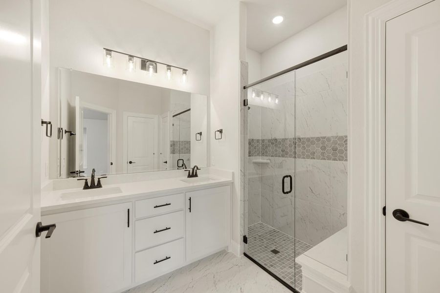 Bathroom with double vanity, white cabinets, and glass-enclosed walk-in shower with marble tile walls