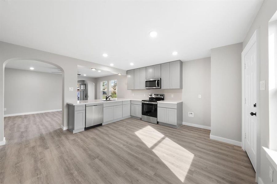 Kitchen with stainless steel appliances, arched walkways, gray cabinetry, open floor plan, and recessed lighting Kitchen with stainless steel appliances, arched walkways, gray cabinetry, open floor plan, and recessed lighting