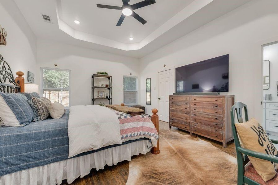 Bedroom with wood finished floors, multiple windows, recessed lighting, ceiling fan, and a tray ceiling