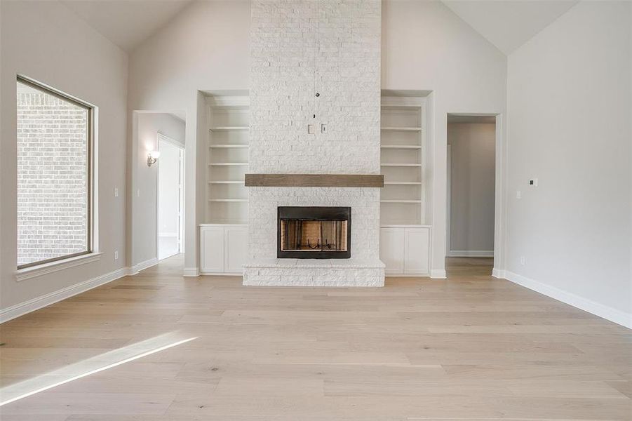 Unfurnished living room with a fireplace, high vaulted ceiling, light hardwood / wood-style flooring, and built in features