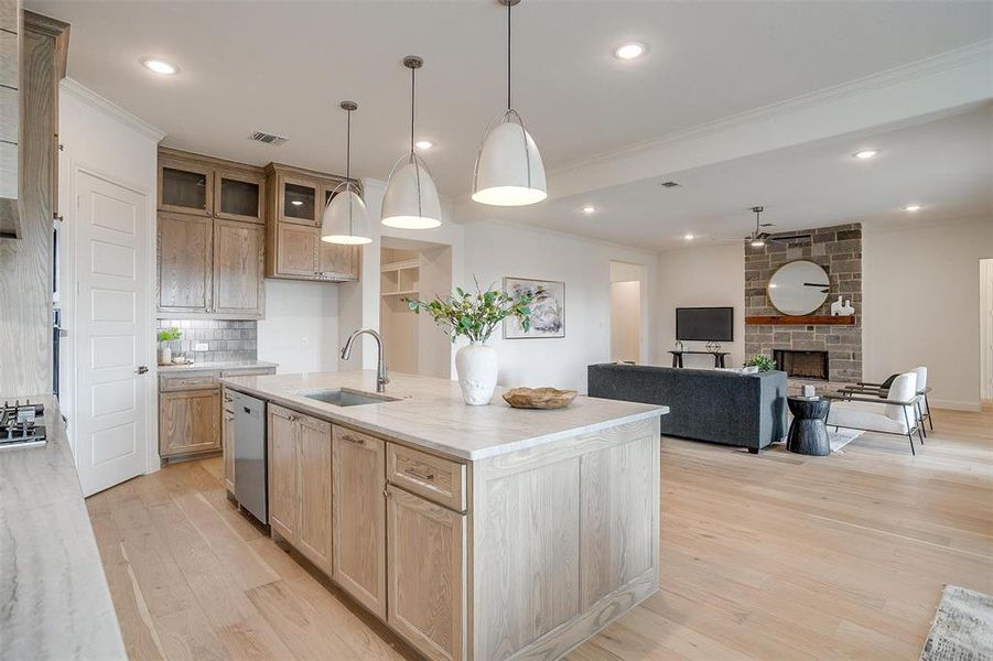 Kitchen featuring light hardwood flooring, a kitchen island with leathered Quartzite countertops, farm sink, natural stain custom cabinetry with soft close drawers and cabinets.