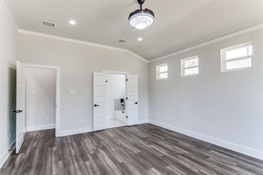 Unfurnished bedroom featuring ensuite bathroom, lofted ceiling, crown molding, and hardwood / wood-style floors