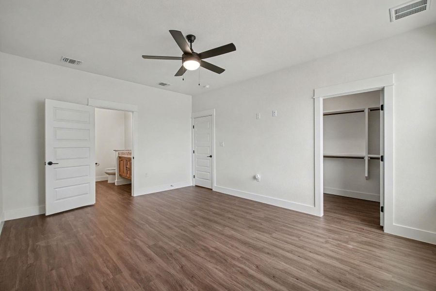 Unfurnished bedroom with a walk in closet, dark wood finished floors, a ceiling fan, and ensuite bath