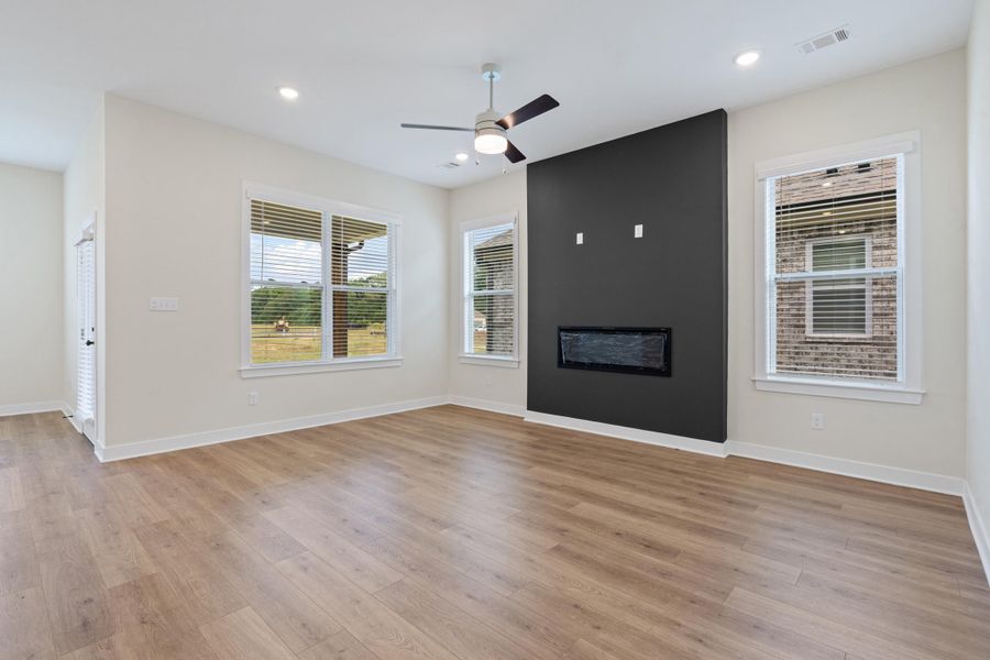 Living area featuring wood-finish flooring, an accent wall with a built-in electric fireplace, a ceiling fan with integrated lighting, and recessed ceiling lights Living area featuring wood-finish flooring, an accent wall with a built-in electric fireplace, a ceiling fan with integrated lighting, and recessed ceiling lights