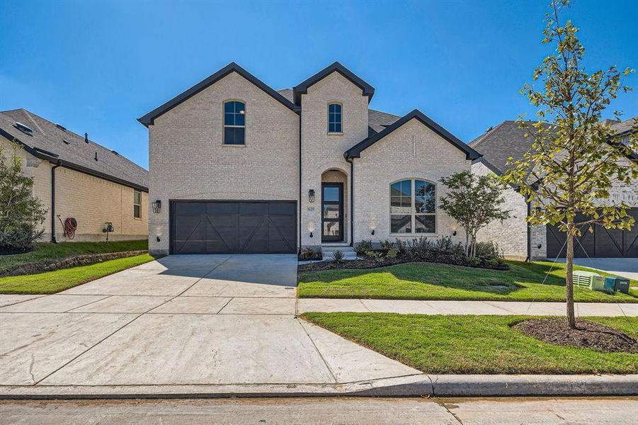 Contemporary two-story residence featuring light-colored brick facade, dark trim, and a prominent front-facing garage with dark paneled doors Contemporary two-story residence featuring light-colored brick facade, dark trim, and a prominent front-facing garage with dark paneled doors