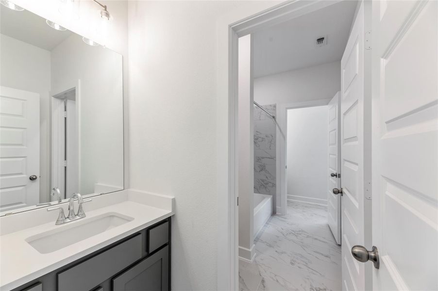 Bathroom featuring light marble finish floors, vanity, and bathing tub / shower combination Bathroom featuring light marble finish floors, vanity, and bathing tub / shower combination
