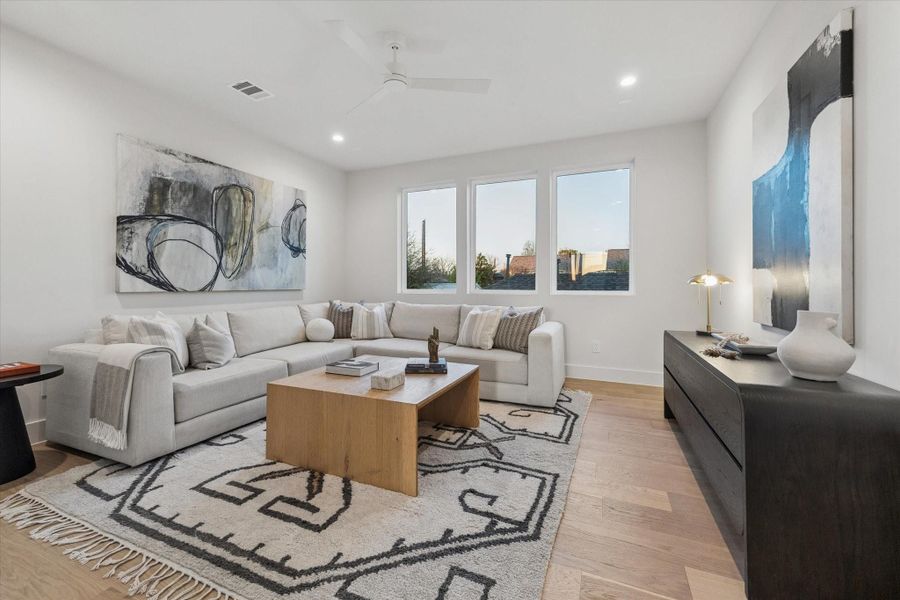 Spacious gameroom with recessed lighting, three picture windows and engineered hardwood floors.