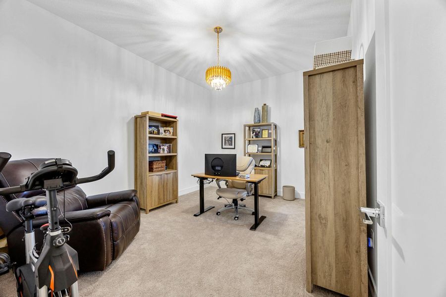 Home office with light colored carpet and a chandelier