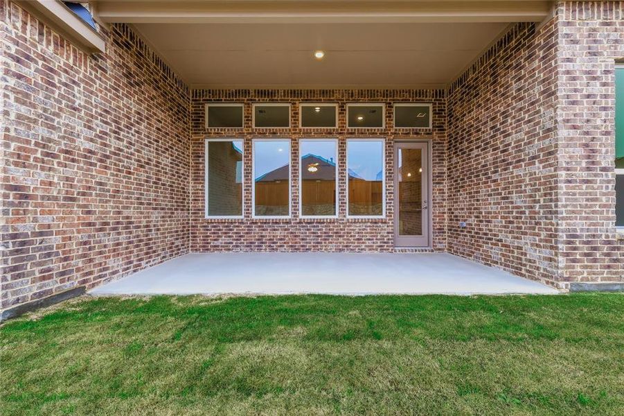 View of exterior entry with brick siding, a patio, and a lawn