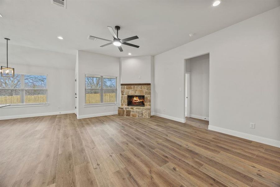 Unfurnished living room with light wood-style flooring, a stone fireplace, a ceiling fan, and recessed lighting Unfurnished living room with light wood-style flooring, a stone fireplace, a ceiling fan, and recessed lighting