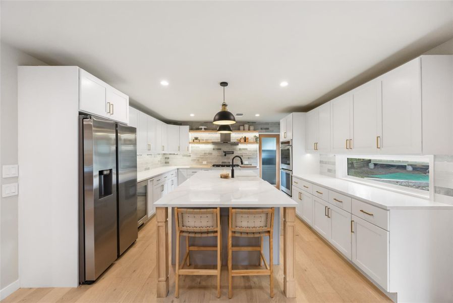 Kitchen featuring stainless steel appliances, white cabinetry, a center island with sink, light stone counters, and pendant lighting