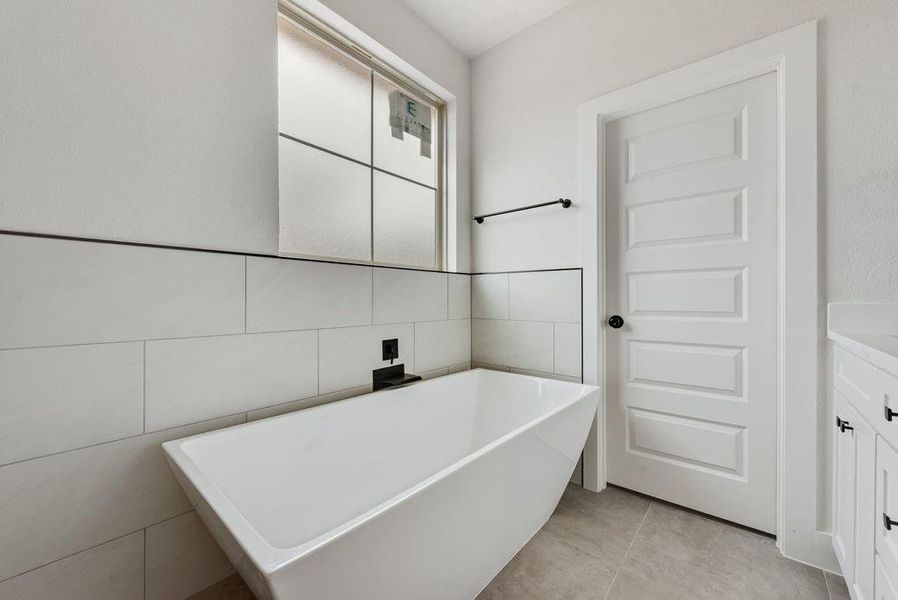 Bathroom with a freestanding tub, vanity, tile walls, and light tile patterned floors