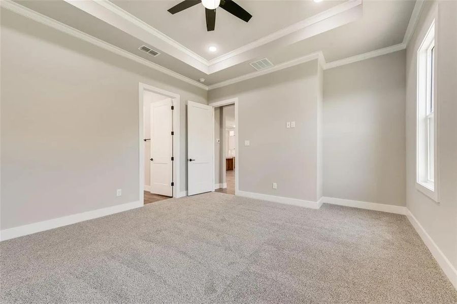 Unfurnished bedroom featuring a tray ceiling, light colored carpet, multiple windows, ceiling fan, and crown molding