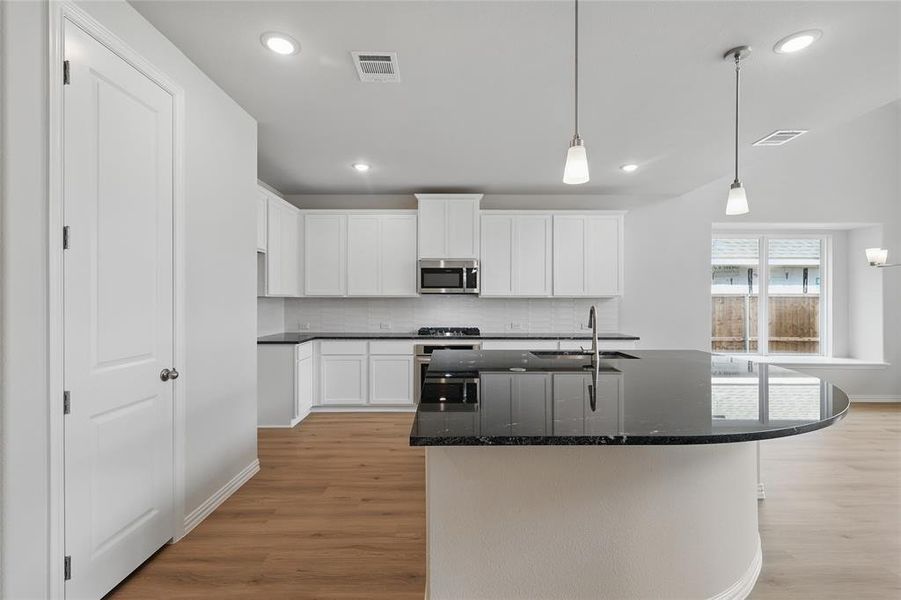 Kitchen with dark stone countertops, an island with sink, white cabinets, and light wood-style flooring