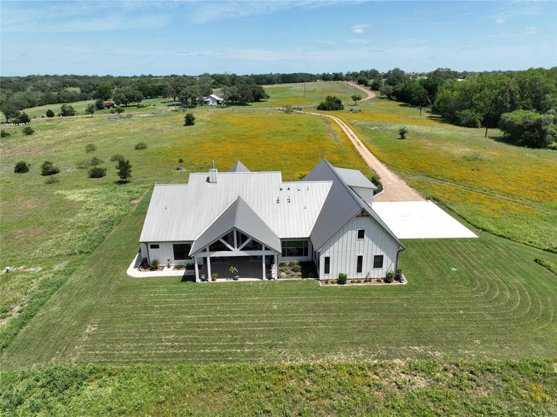 An aerial perspective reveals a contemporary farmhouse set amidst vast, rolling fields.